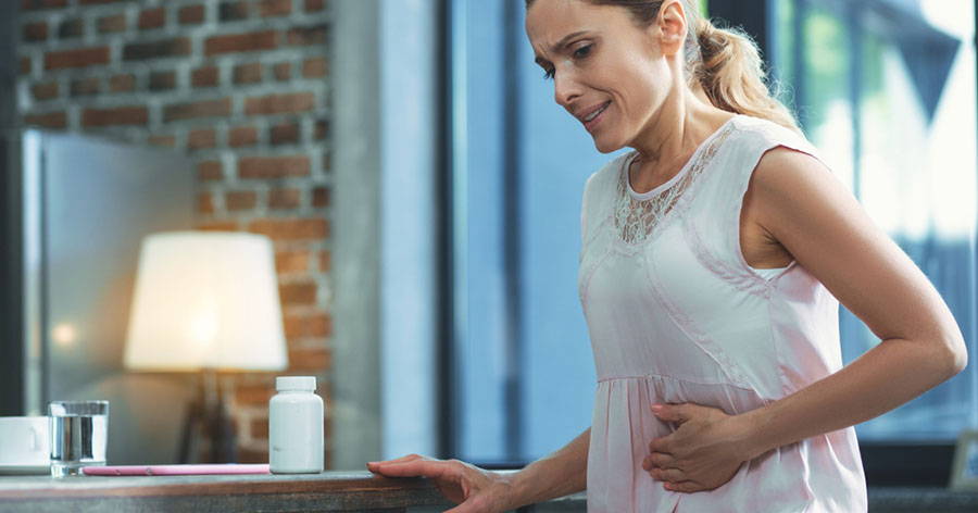 Woman with constipation pain clutching her stomach with her hand as she becomes visibly stressed by the ongoing cramps 