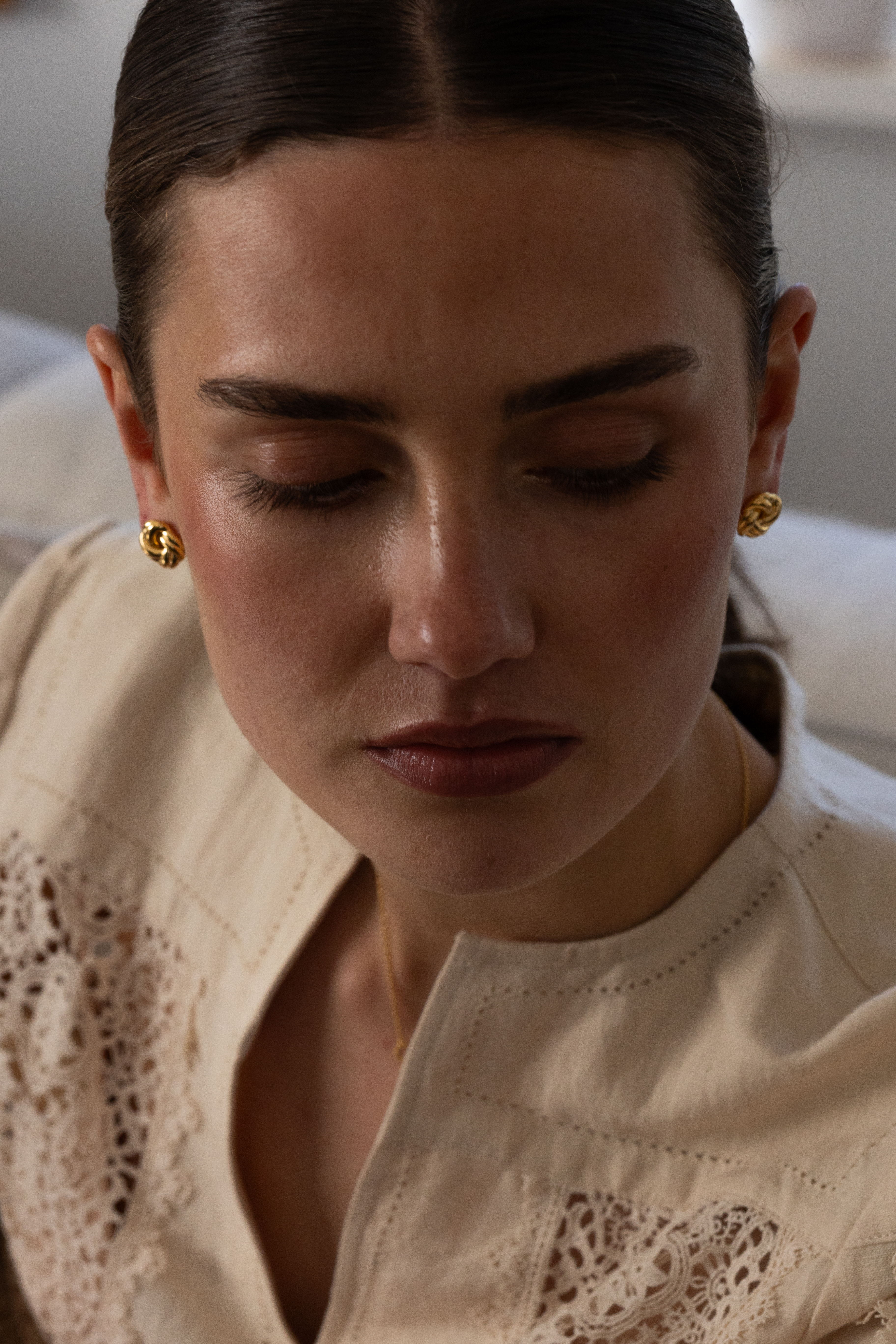 A woman with dark hair wearing gold earrings, looking down thoughtfully.