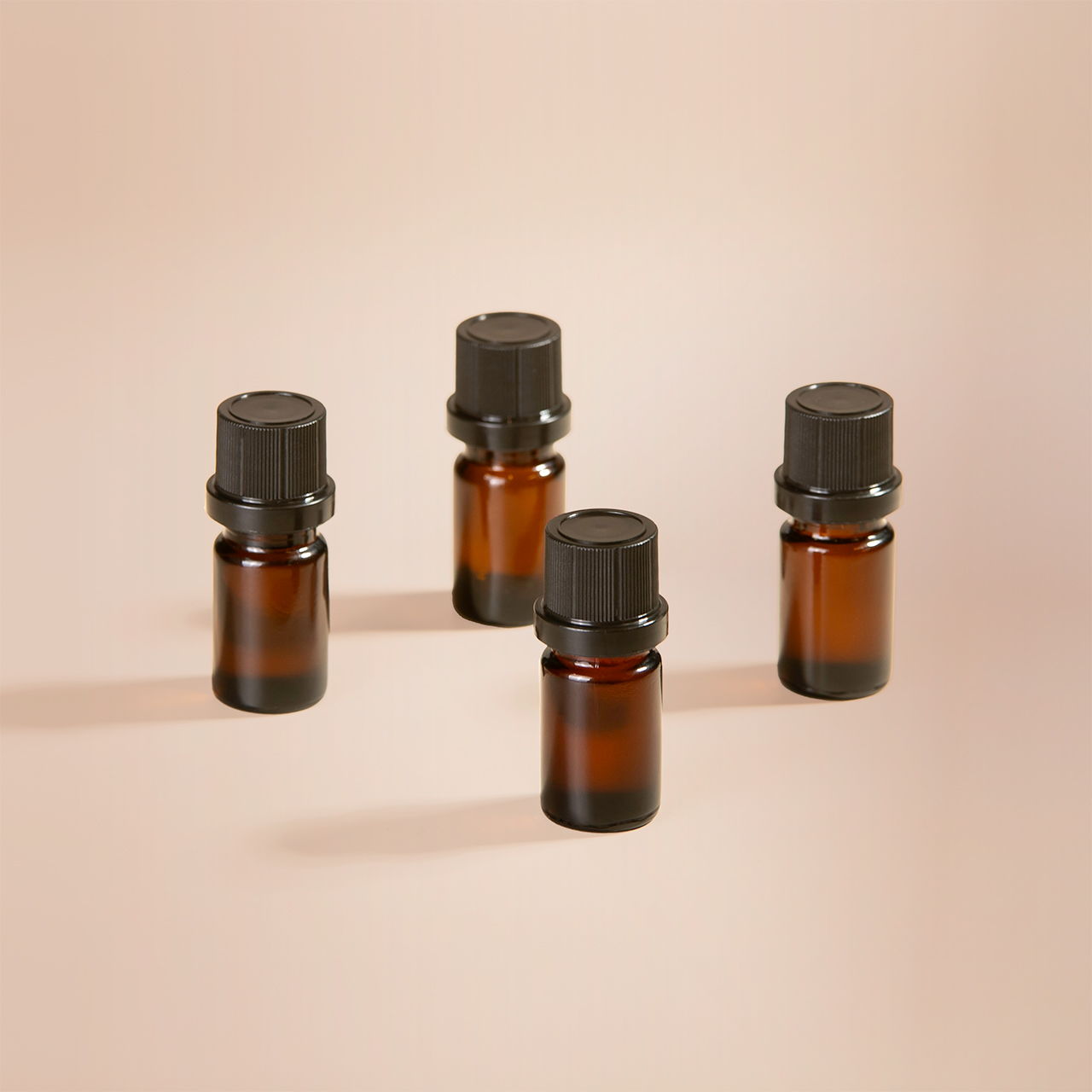 Four amber glass bottles with black caps on a light background.
