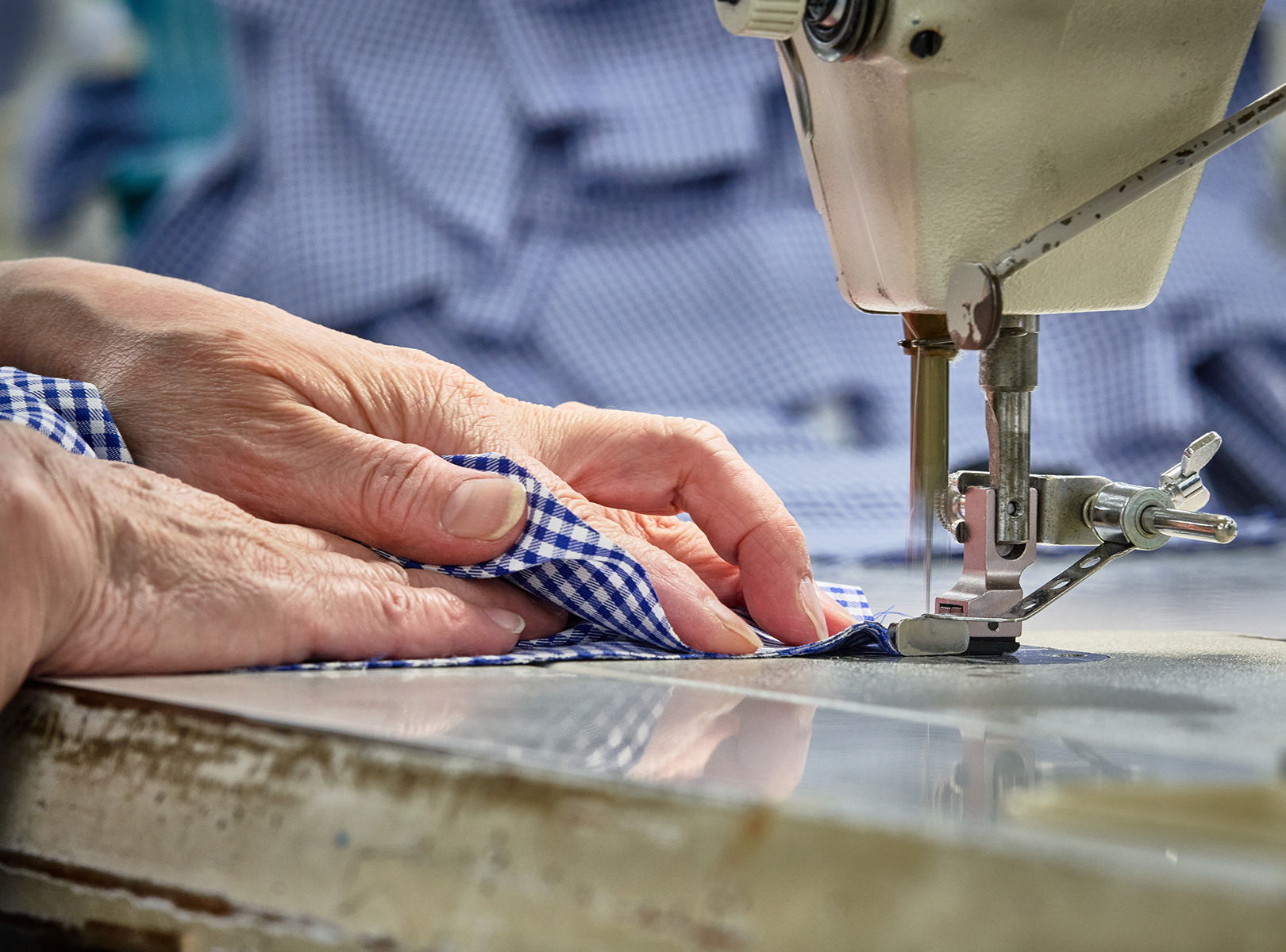Hands guiding fabric through a sewing machine on a work table.