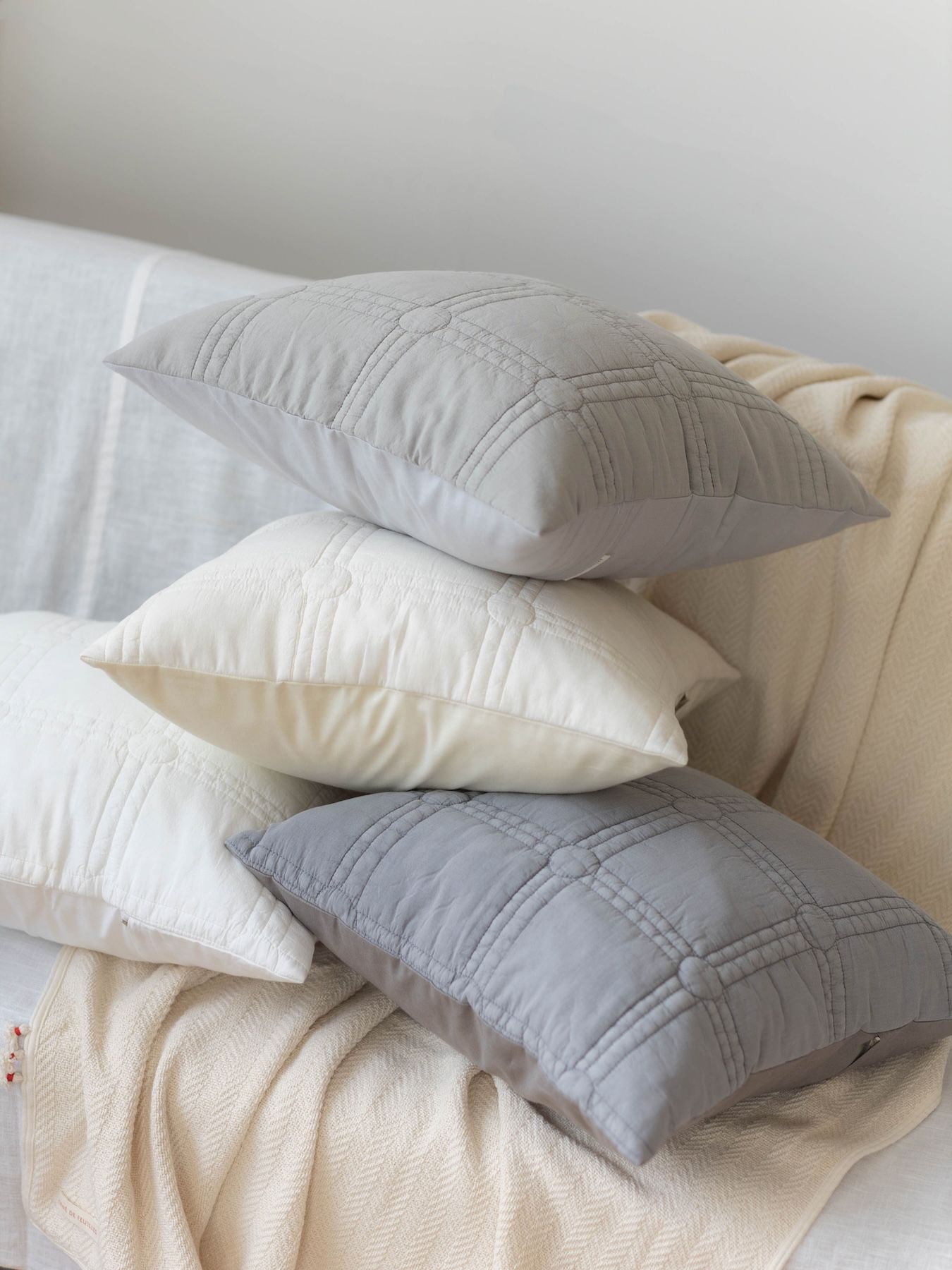 Four decorative pillows stacked on a light-colored blanket.