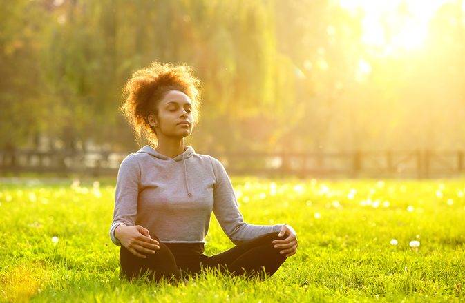 Woman in park sitting crosslegged doing a breathing exercise.