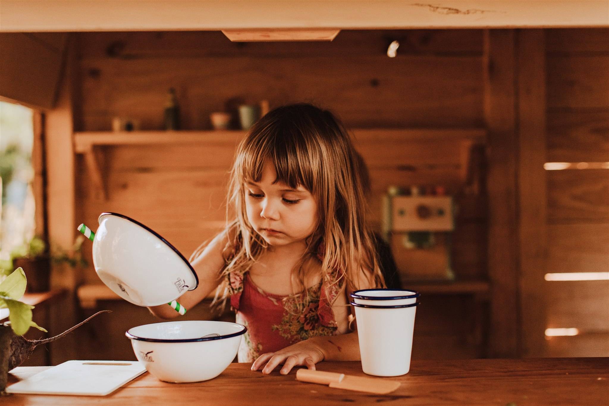 A girl playing with bowls and cups in a cubby house