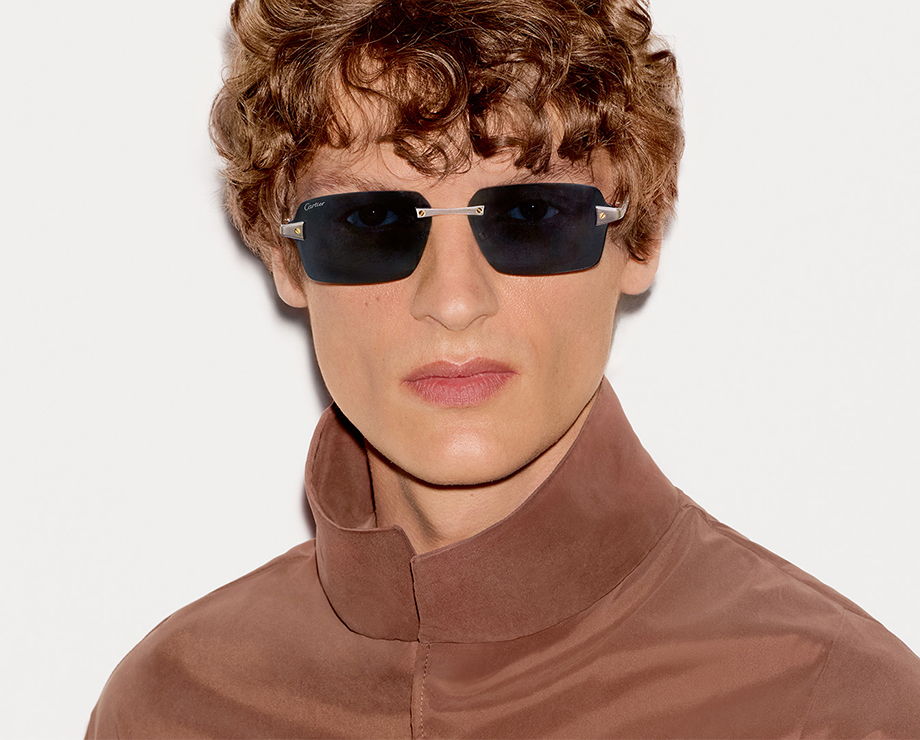 A person with curly hair wearing Cartier sunglasses and a brown jacket.
