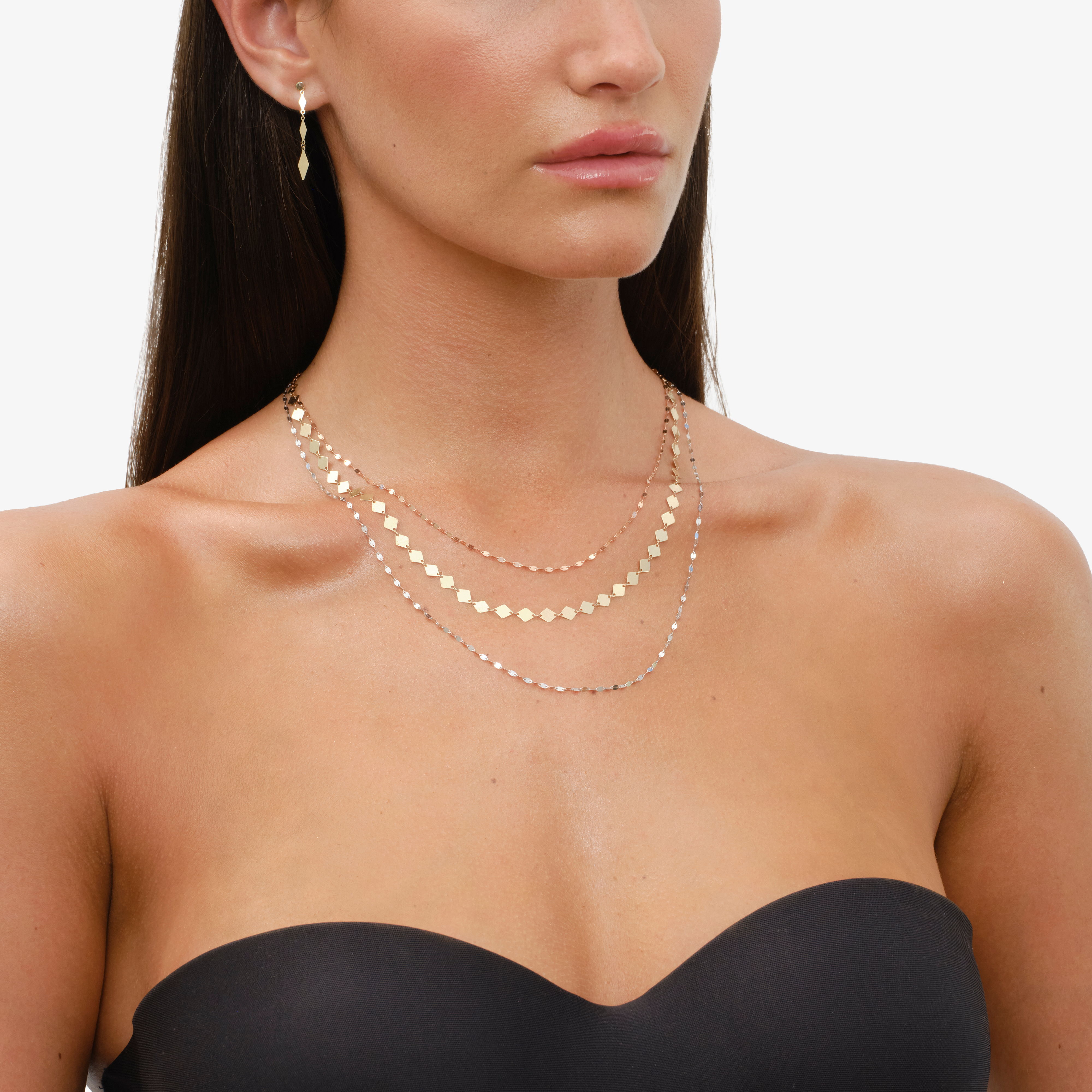 Woman wearing layered gold necklaces and earrings, with a strapless top.