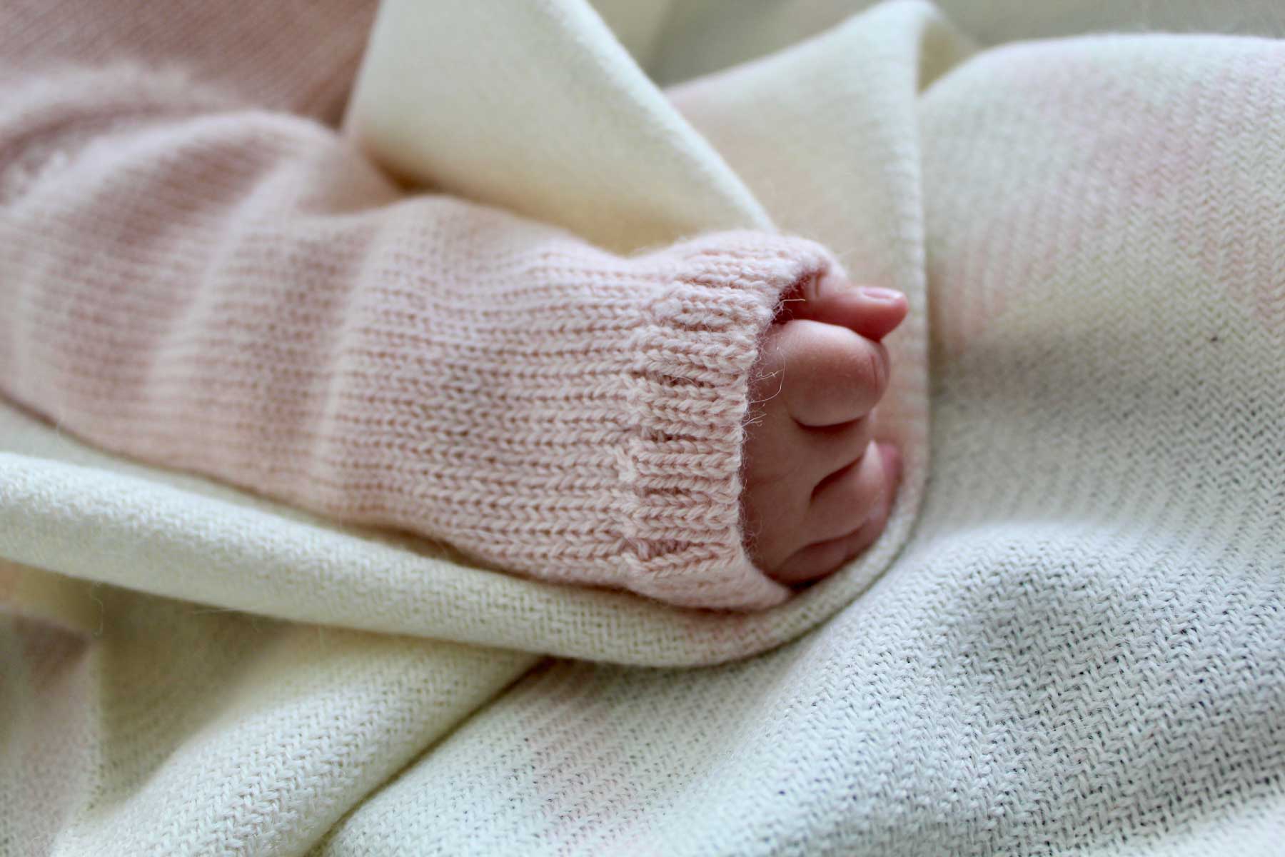 A baby's hand and foot peeking out from a blanket.