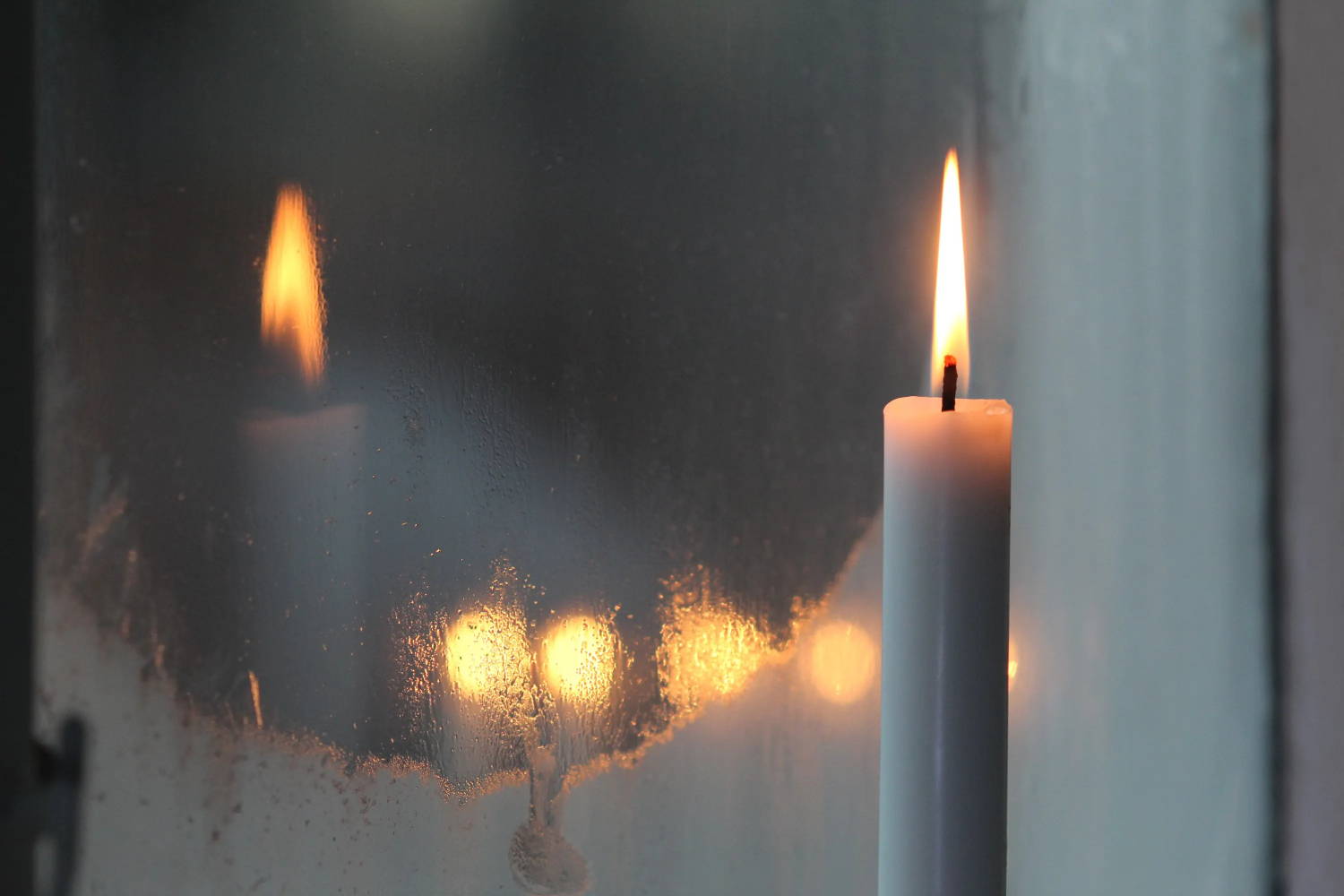 Lit taper candle sitting in a frosty window
