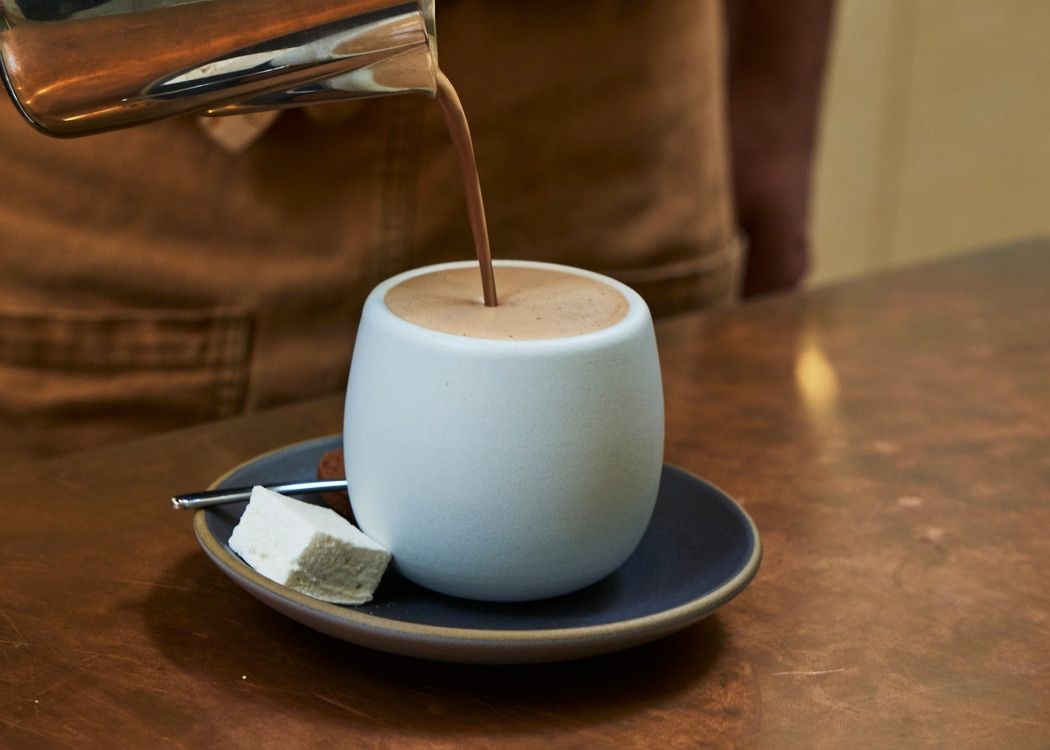 A cup being filled with chocolate drink on a plate with sugar.