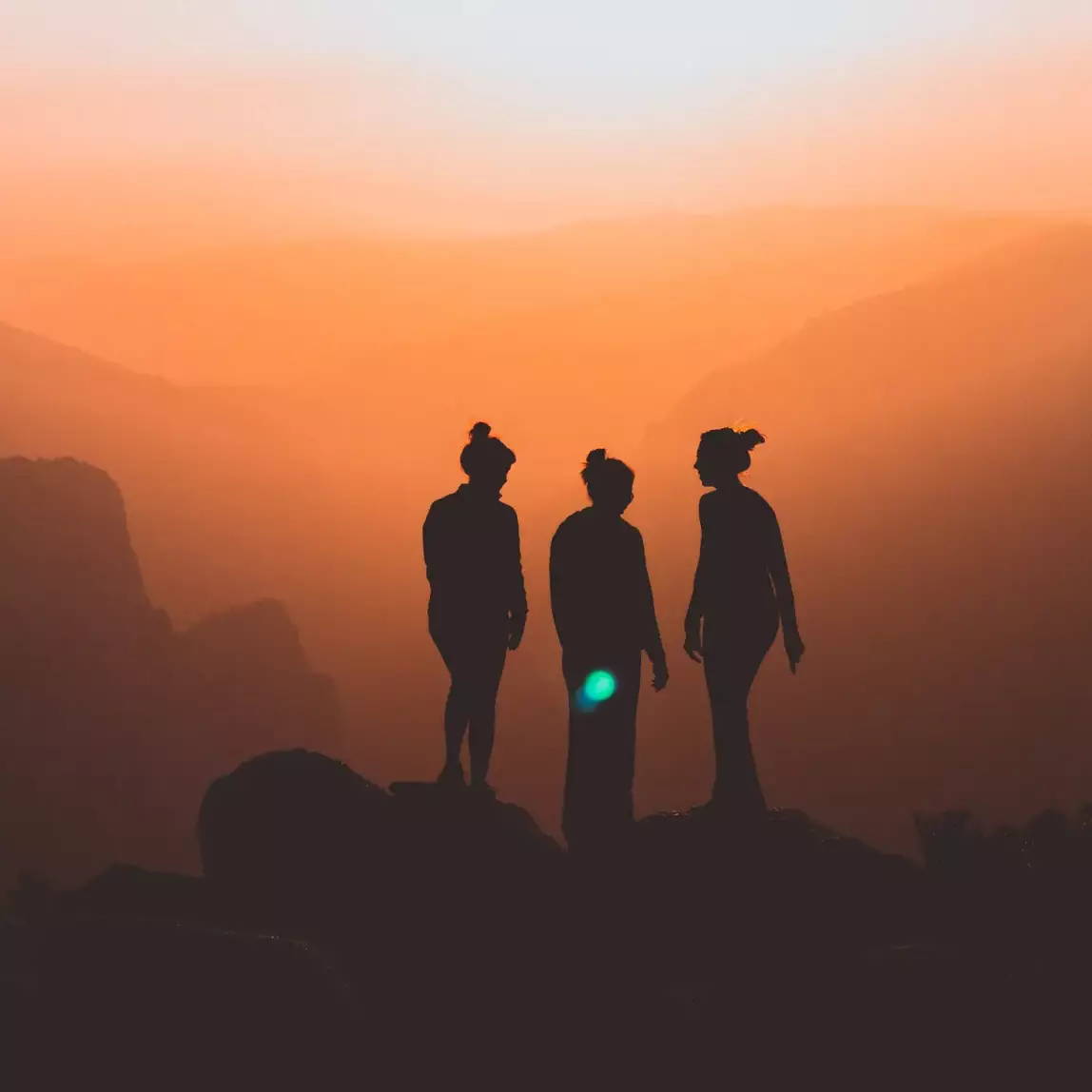 Three silhouettes of women on mountain peak looking out over sunset.