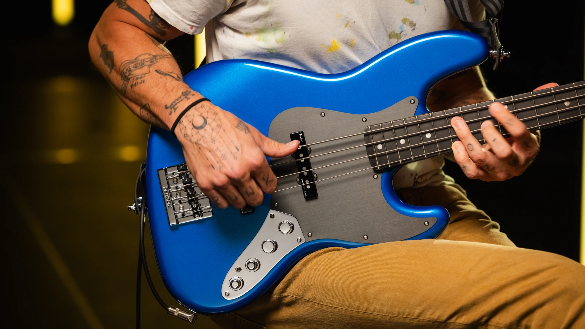 A person playing a blue Fender American Ultra II Jazz Bass guitar.