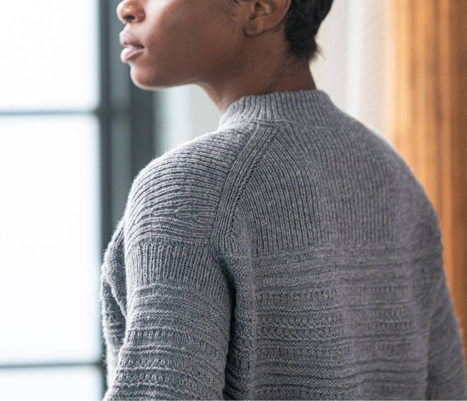 Maya, a woman with short hair. models Brooklyn Tweed hand knit Grist Pullover in Imbue Sport color Ash -- back shoulder view