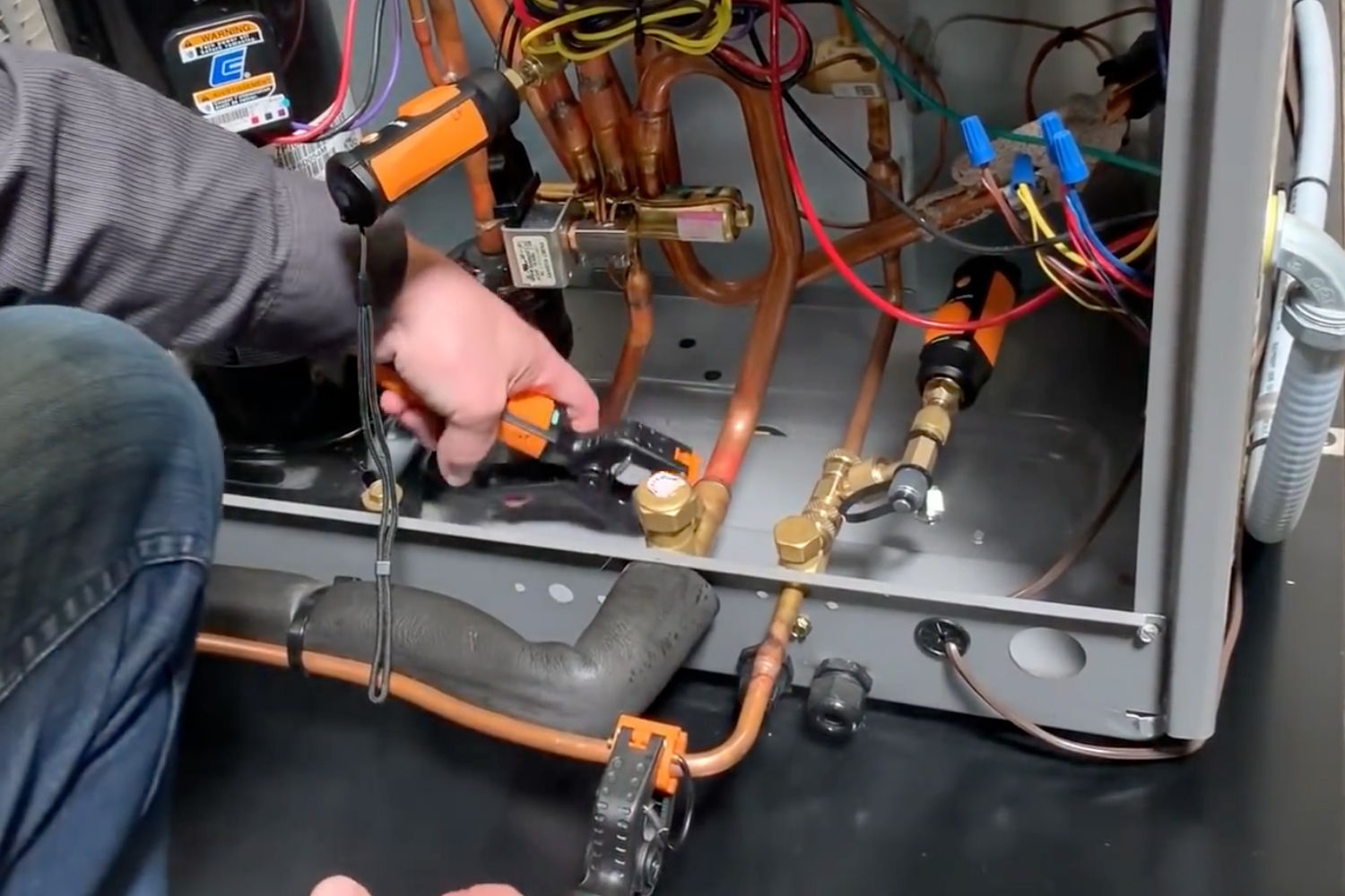 Person using tools on copper pipes inside an appliance.