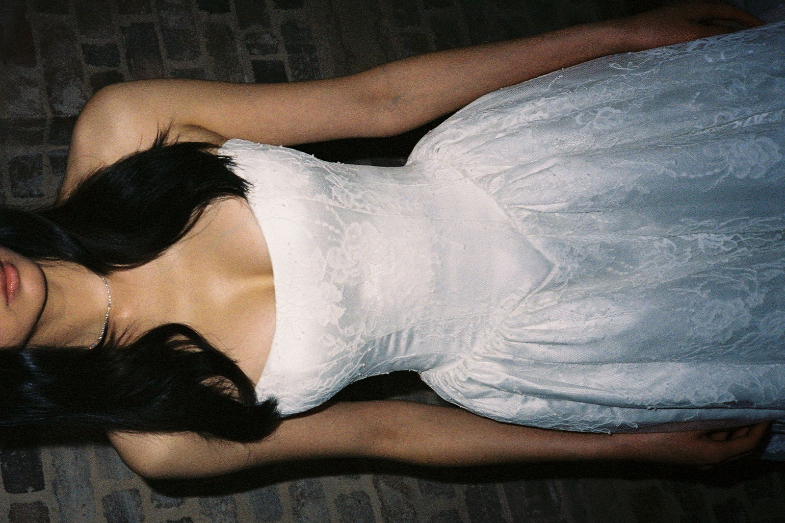 Woman wearing a white dress against a brick wall background.