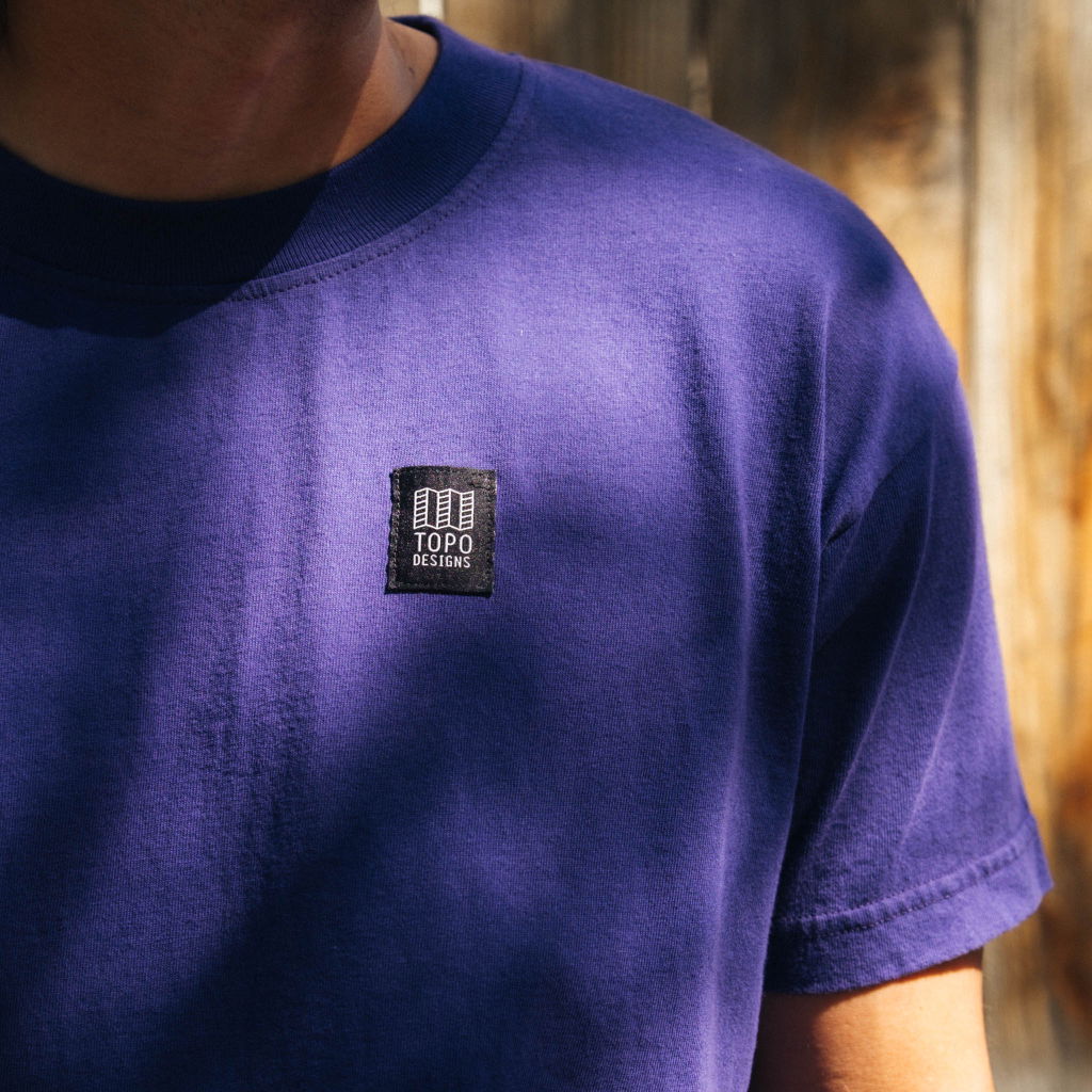 Person wearing a purple t-shirt with a black logo patch.