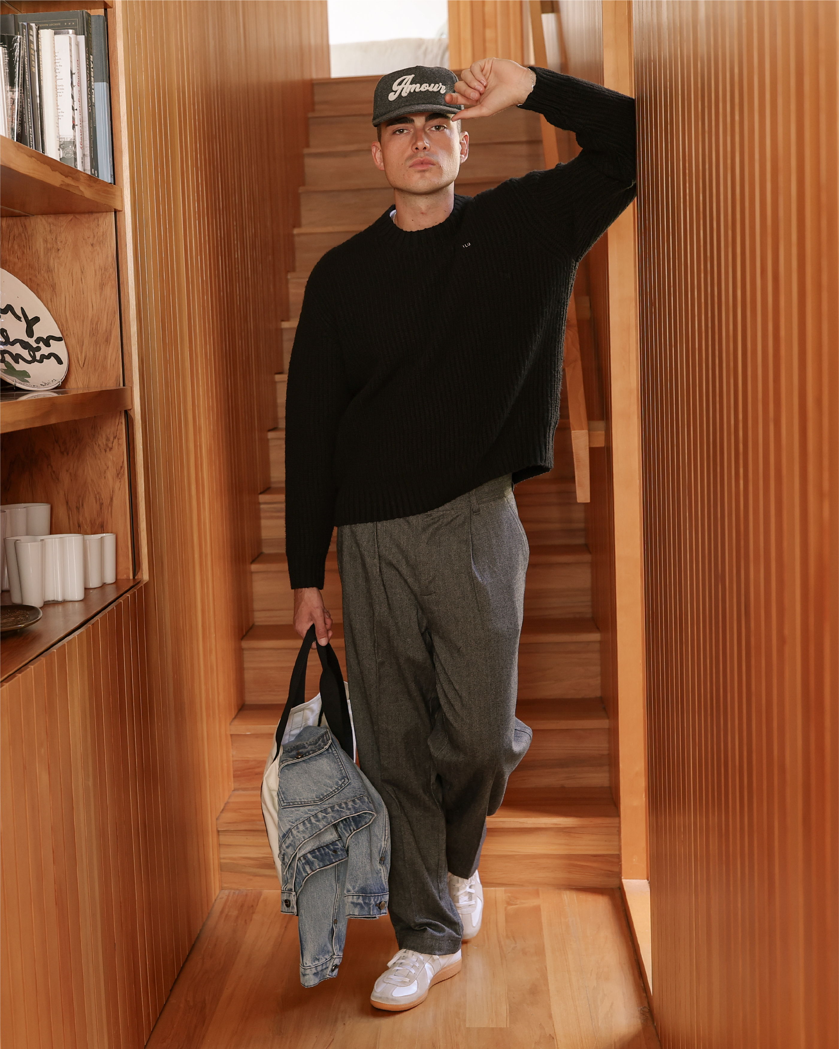 Person walking in a hallway, wearing a black sweater and holding a bag.