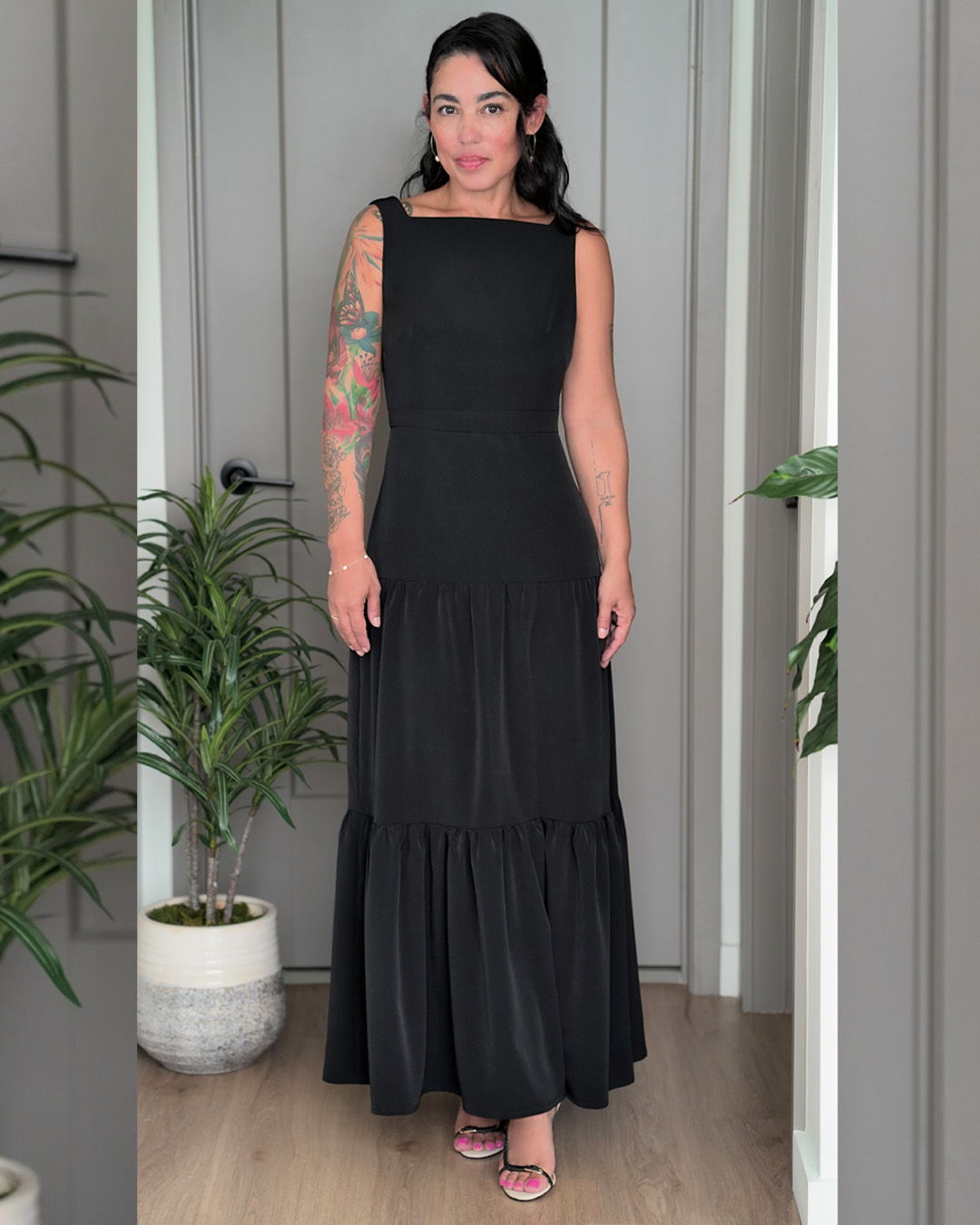 Woman in a black dress standing in a room with plants.