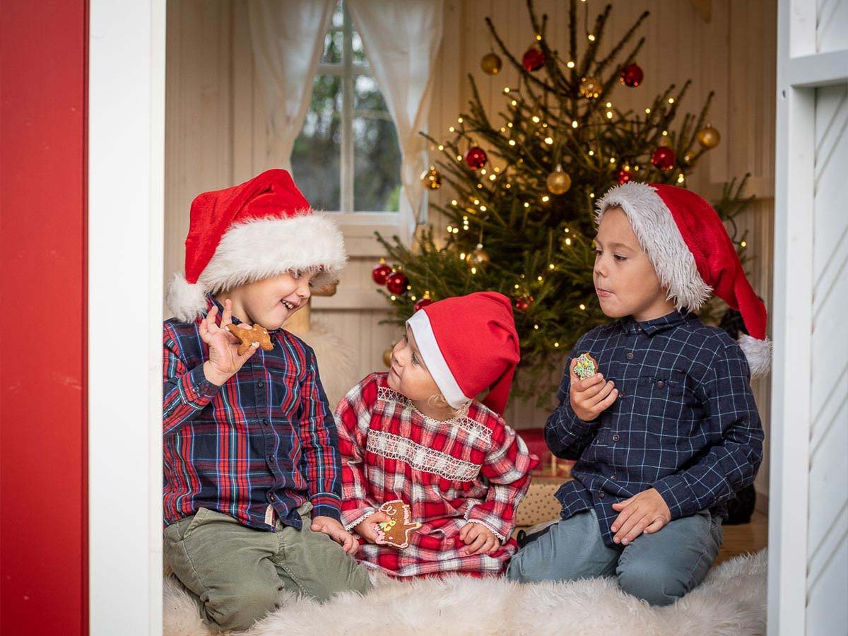 Kids in elf hats eat gingerbread in Red Wooden Playhouse Nordic Nario by WholeWoodPlayhouses