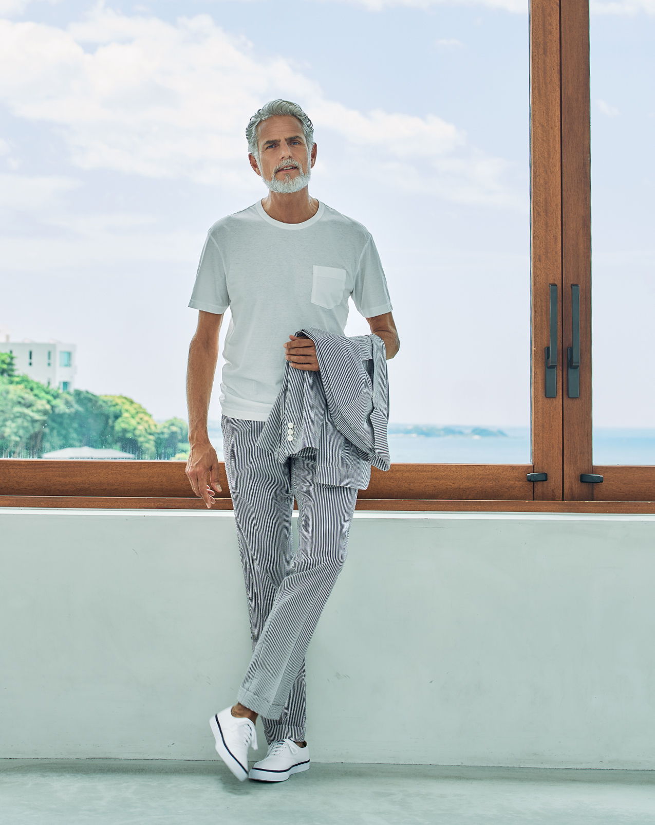 Man in casual attire leaning against a wall with a view of the ocean.