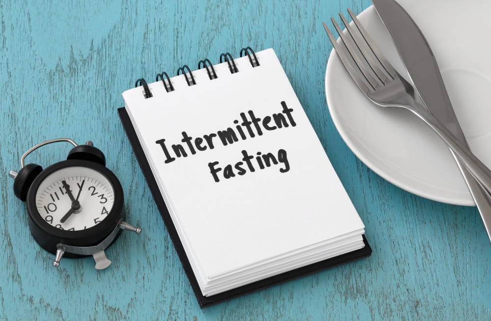 intermittent fasting word on notebook with clock fork knife on white plate|The Intermittent Fasting Guide For Optimal Health