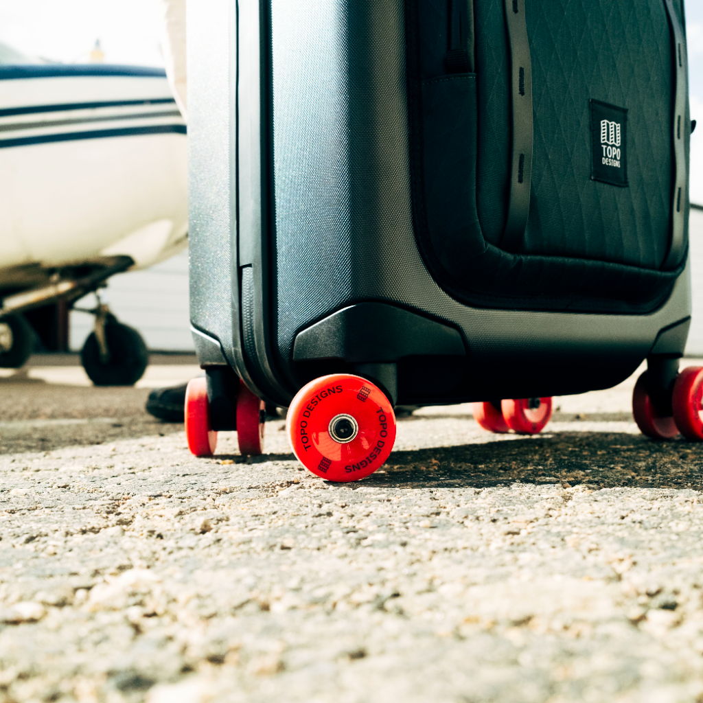 A suitcase with red wheels on a runway near an airplane.