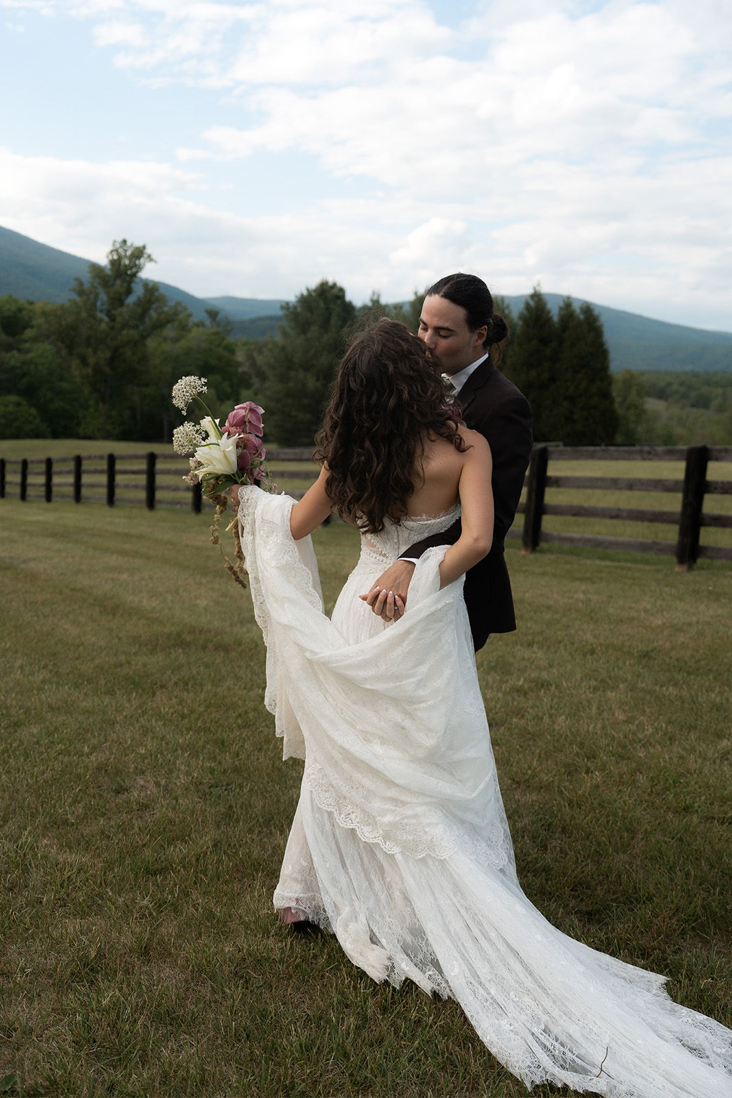 A couple in wedding attire embracing in a grassy field.