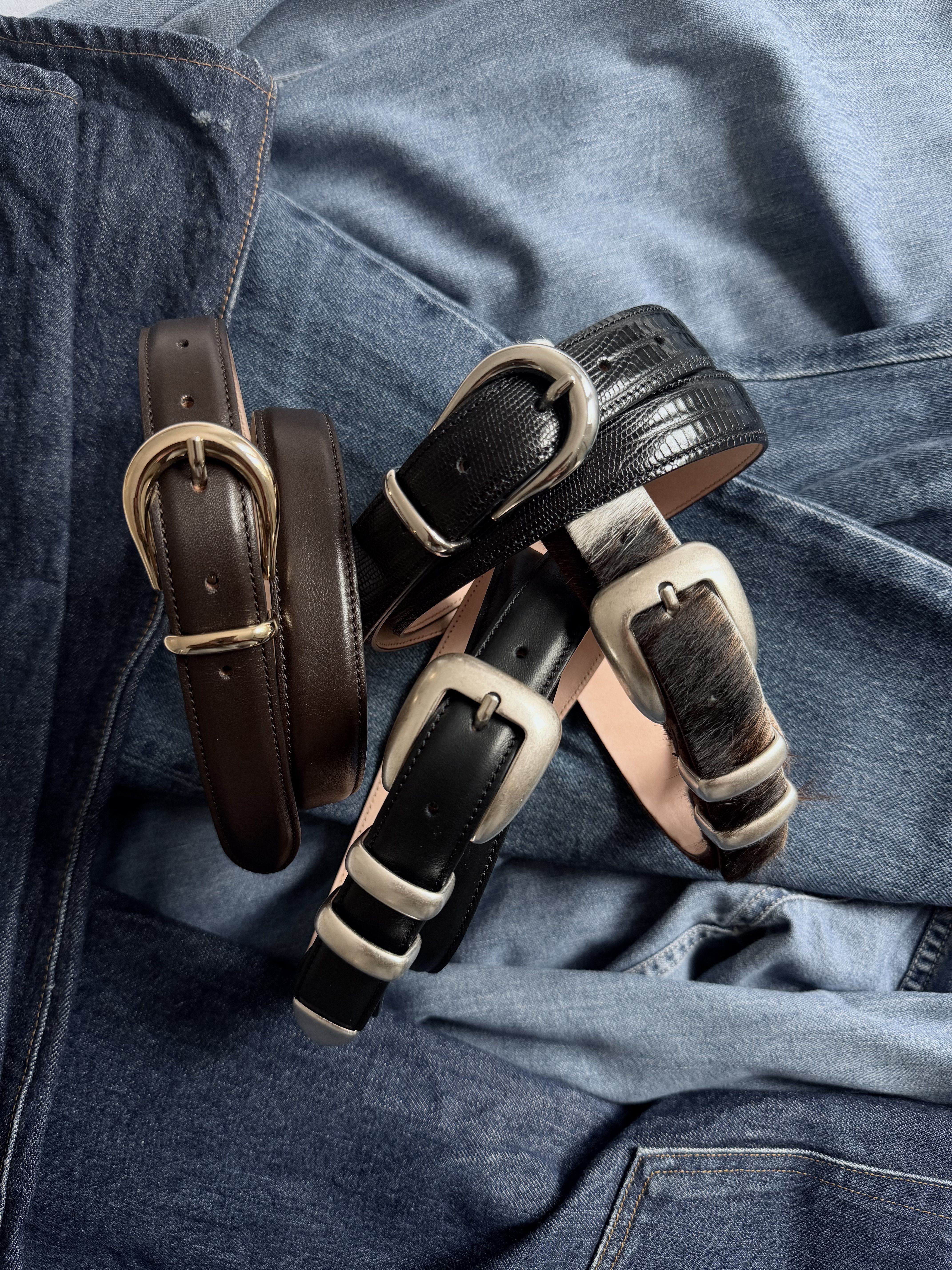 Several leather belts arranged on denim fabric.