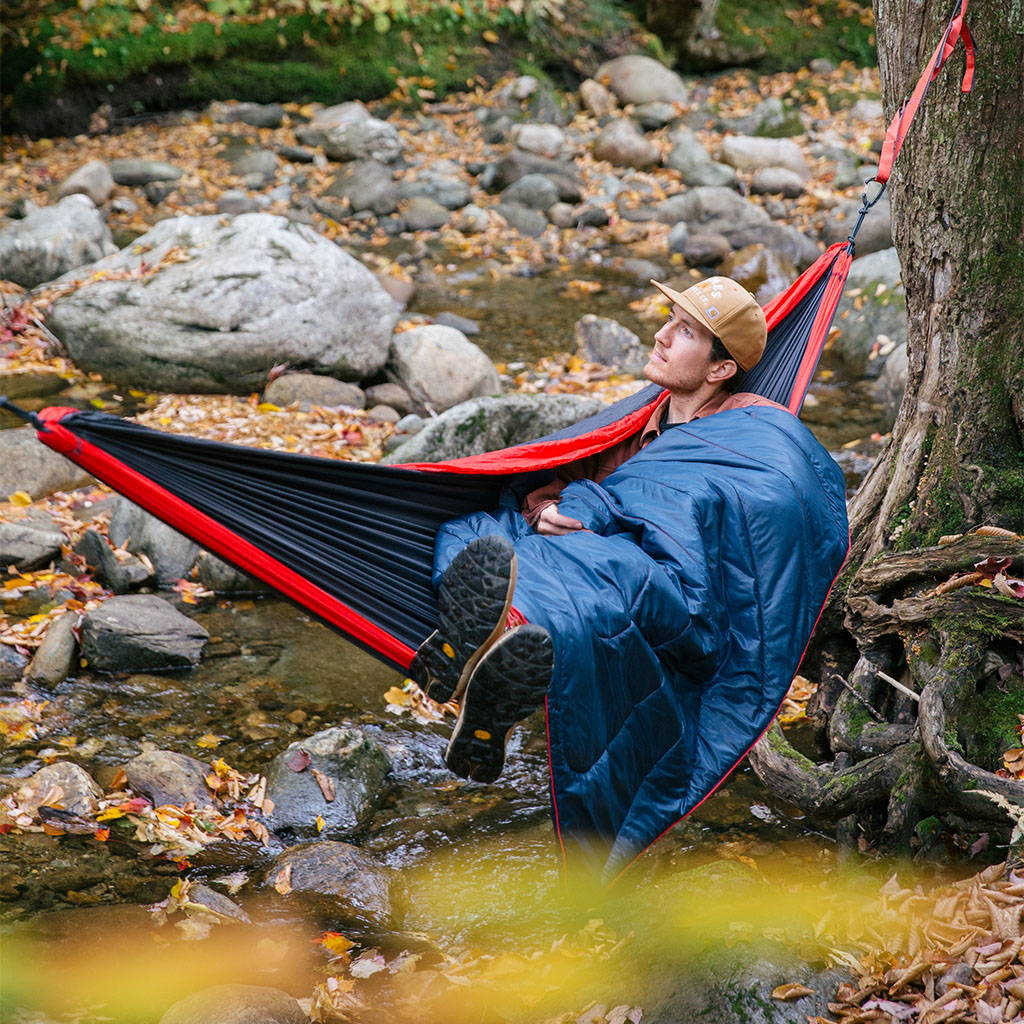 A man sits in his hammock enjoying the great outdoors with a Rumpl blanket to keep him warm and cozy.