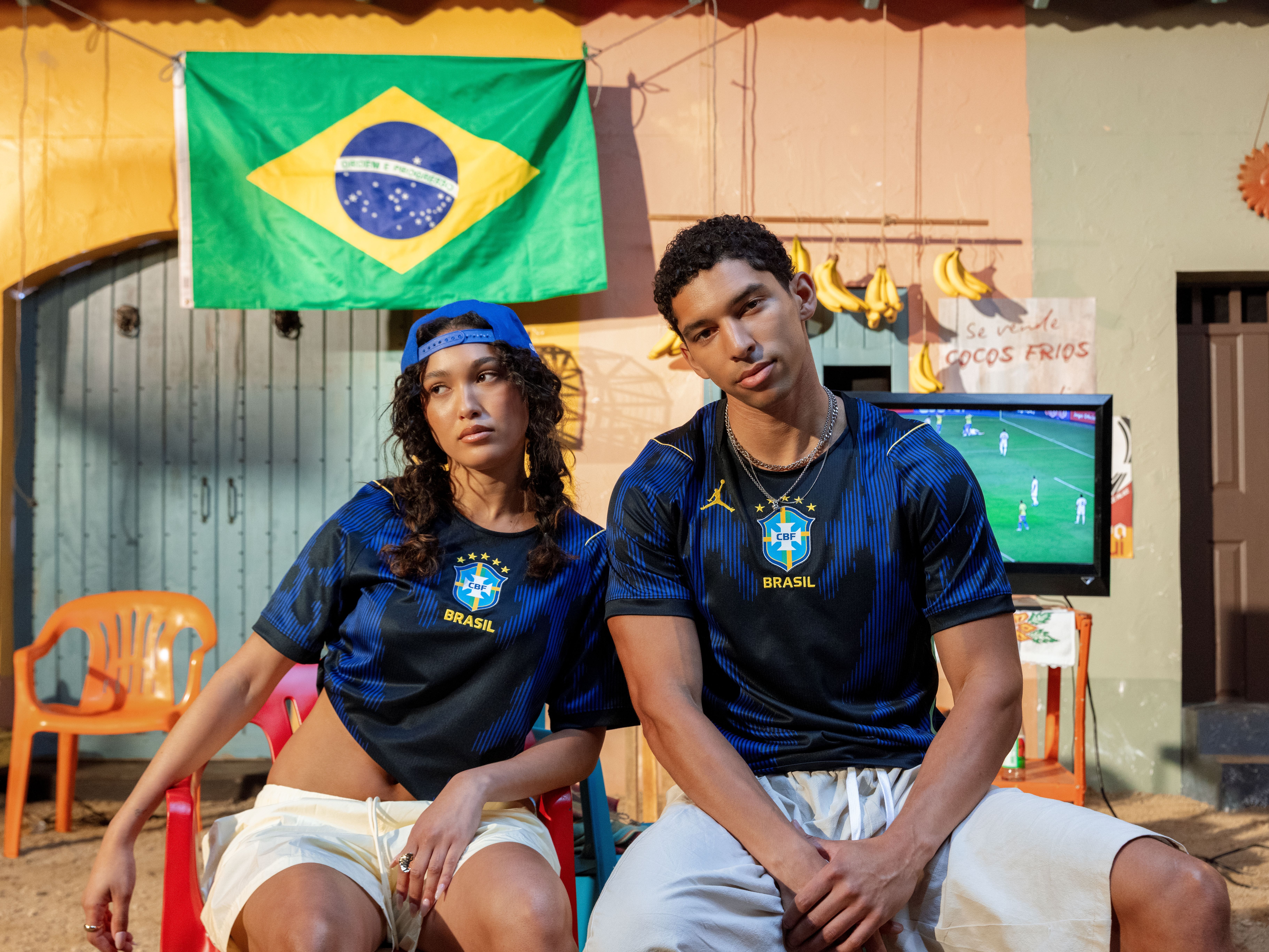 Two people in Brazil jerseys sit in front of a Brazilian flag.