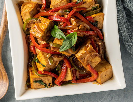 Tofu stir-fry with colorful bell peppers and fresh herbs in a white dish.