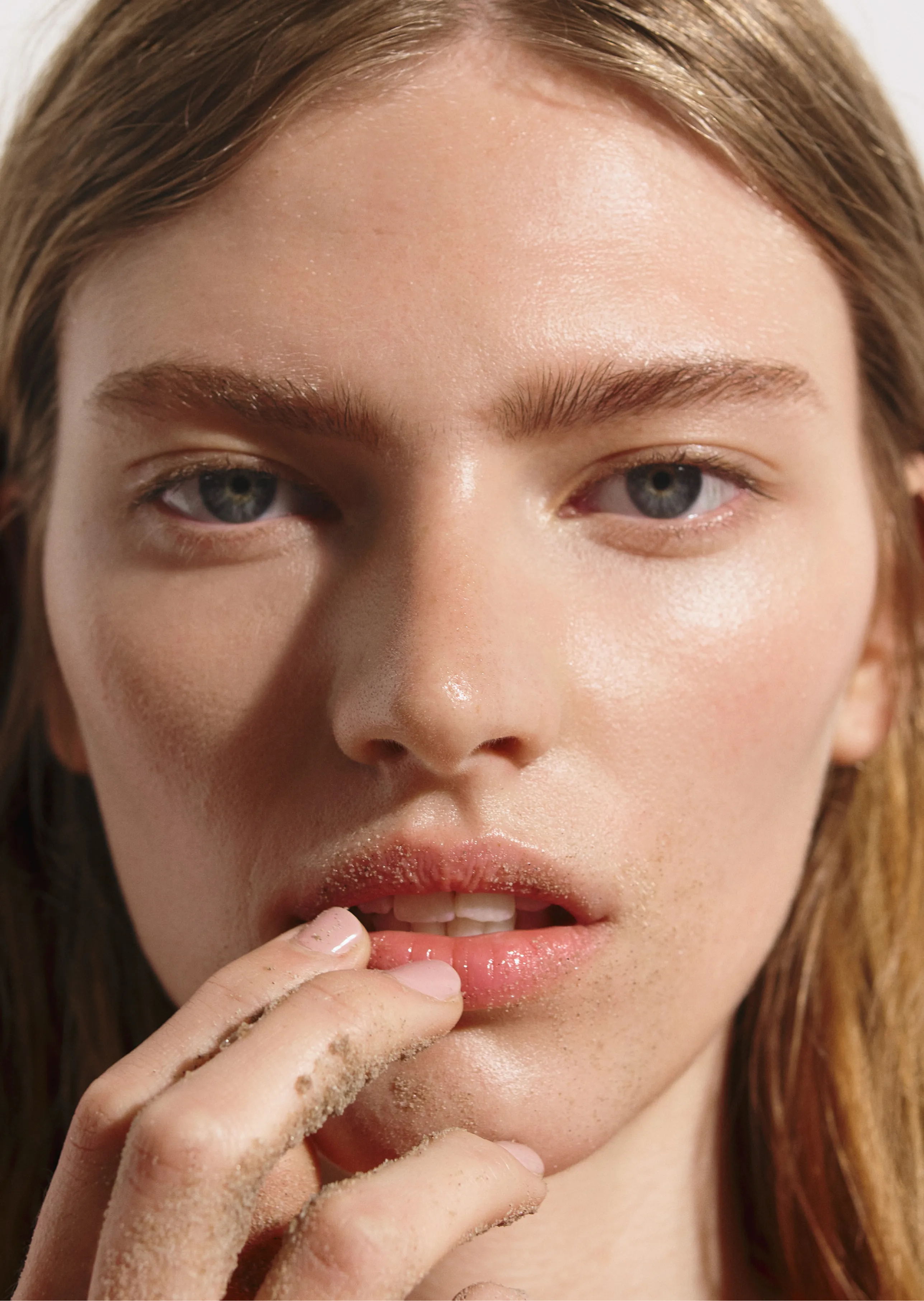 Close-up portrait of a person with long hair touching their lips.