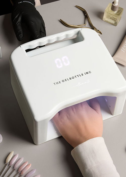 A hand inside a nail curing lamp with surrounding manicure tools.