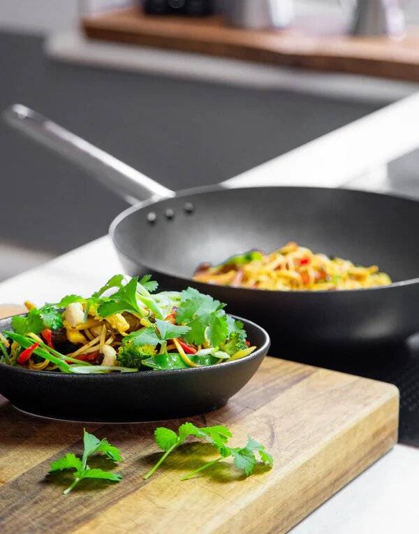 A bowl of stir fry on a chopping board with a wok in the background.