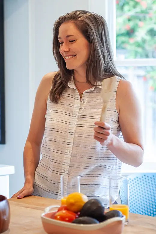 Smiling woman holding a knife in a kitchen with fresh vegetables.