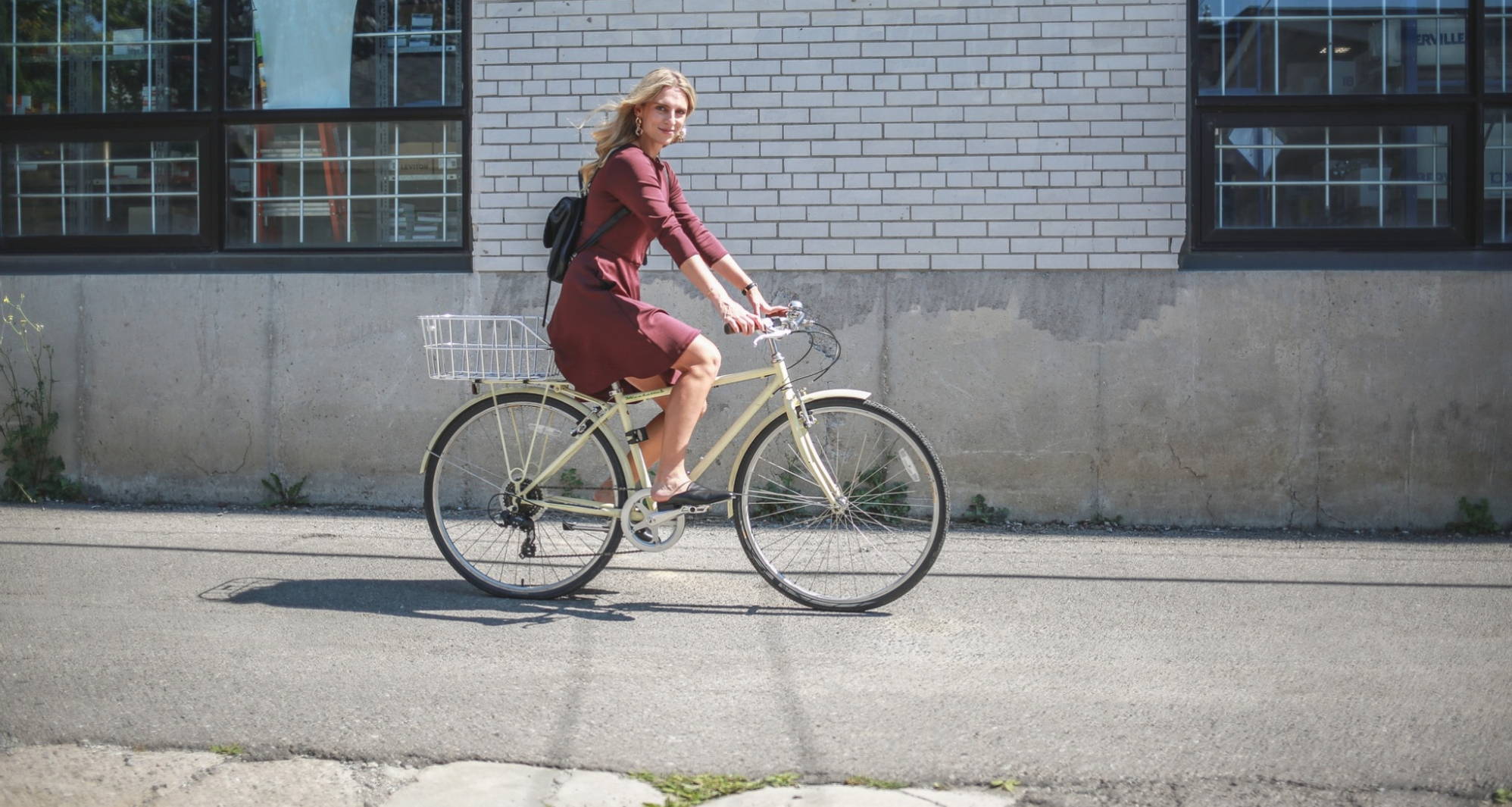 A woman bikes down a city street, wearing a dress from capsule wardrobe brand Encircled.