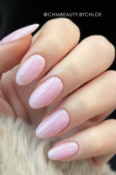 A hand with long, pink, sparkly nails against a soft background.