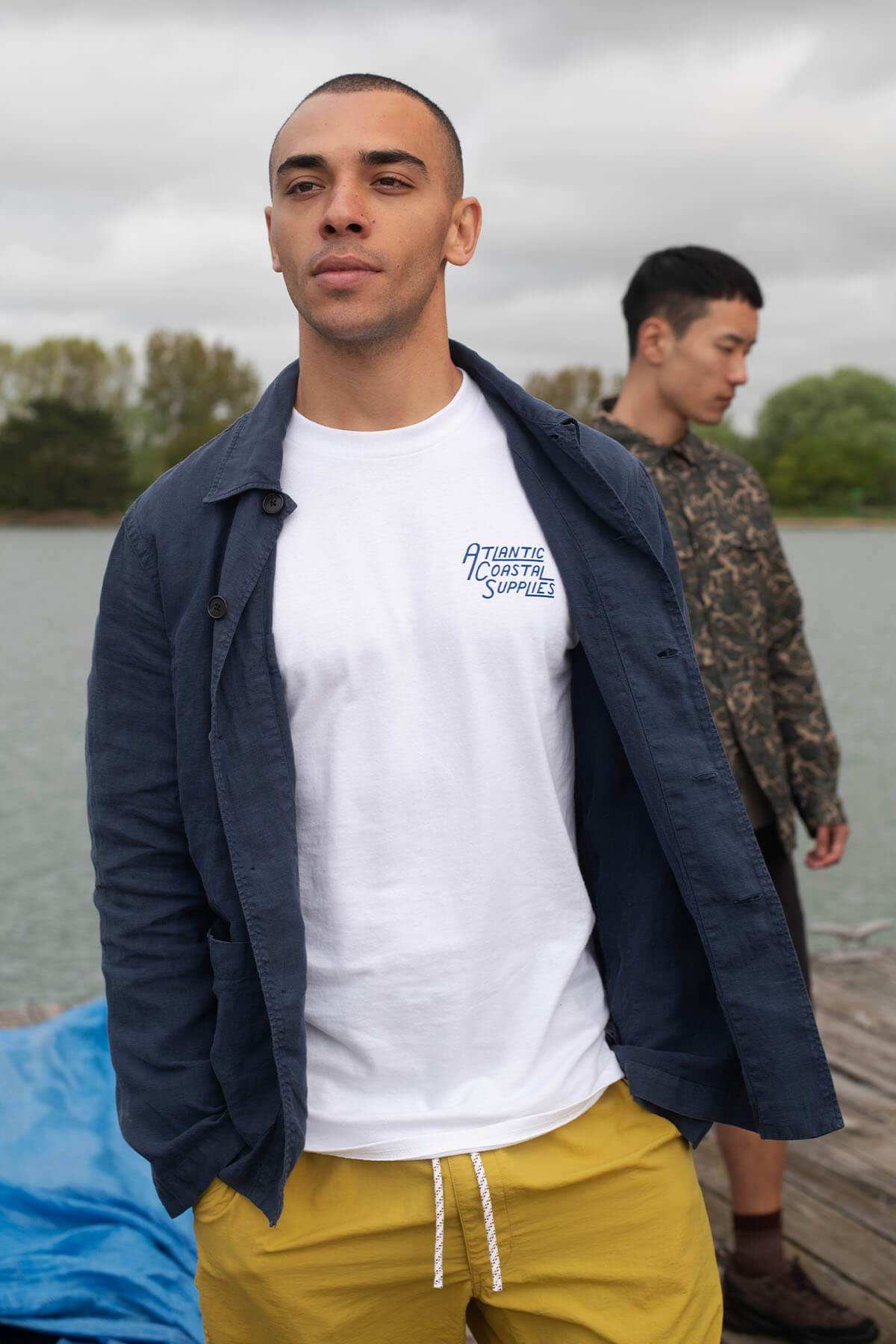 Two men standing near a body of water, one in a white shirt.
