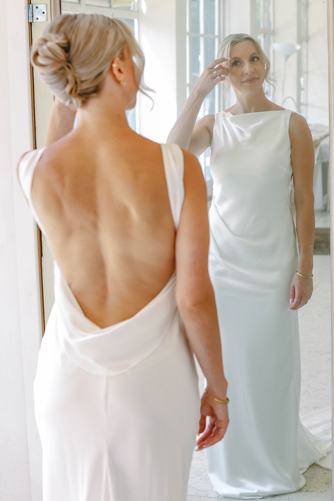 Woman in elegant white dress admiring reflection in a mirror.