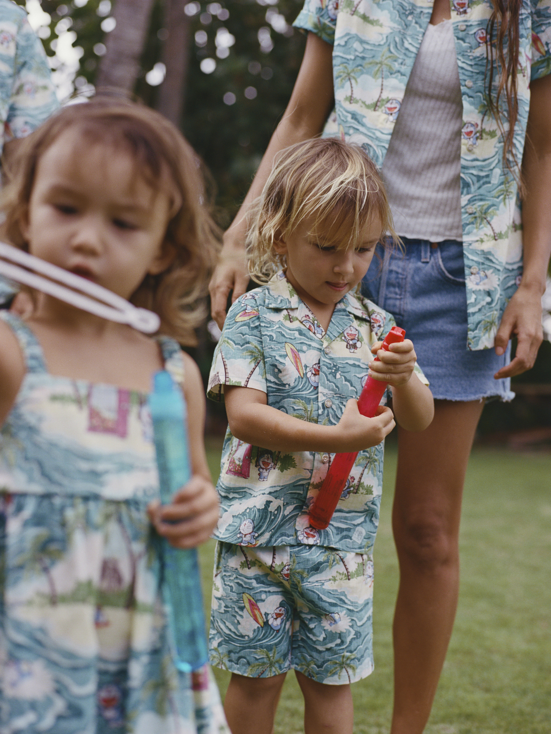 Children playing outside in matching tropical outfits, holding toys.