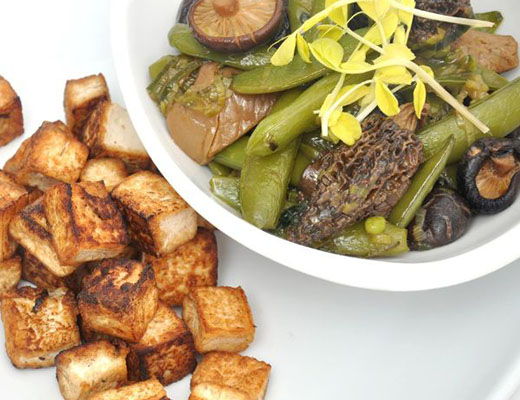 A bowl of vegetables with mushrooms and fried tofu cubes on the side.
