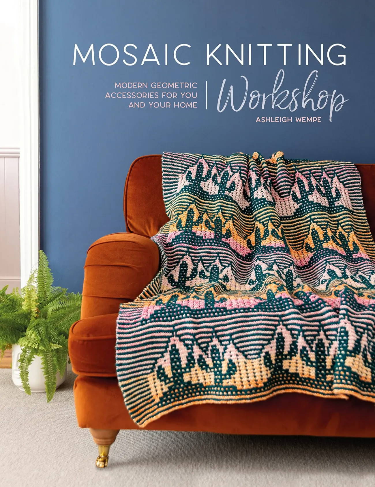 A  book cover titled Mosaic Knitting Workshop by Ashleigh Wempe. There is a  rainbow and green blanket with cactus motifs sitting on a orange chair with a blue wall behind.