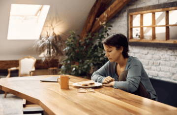 Person sitting at a wooden table, looking pensively at a notebook and mug.