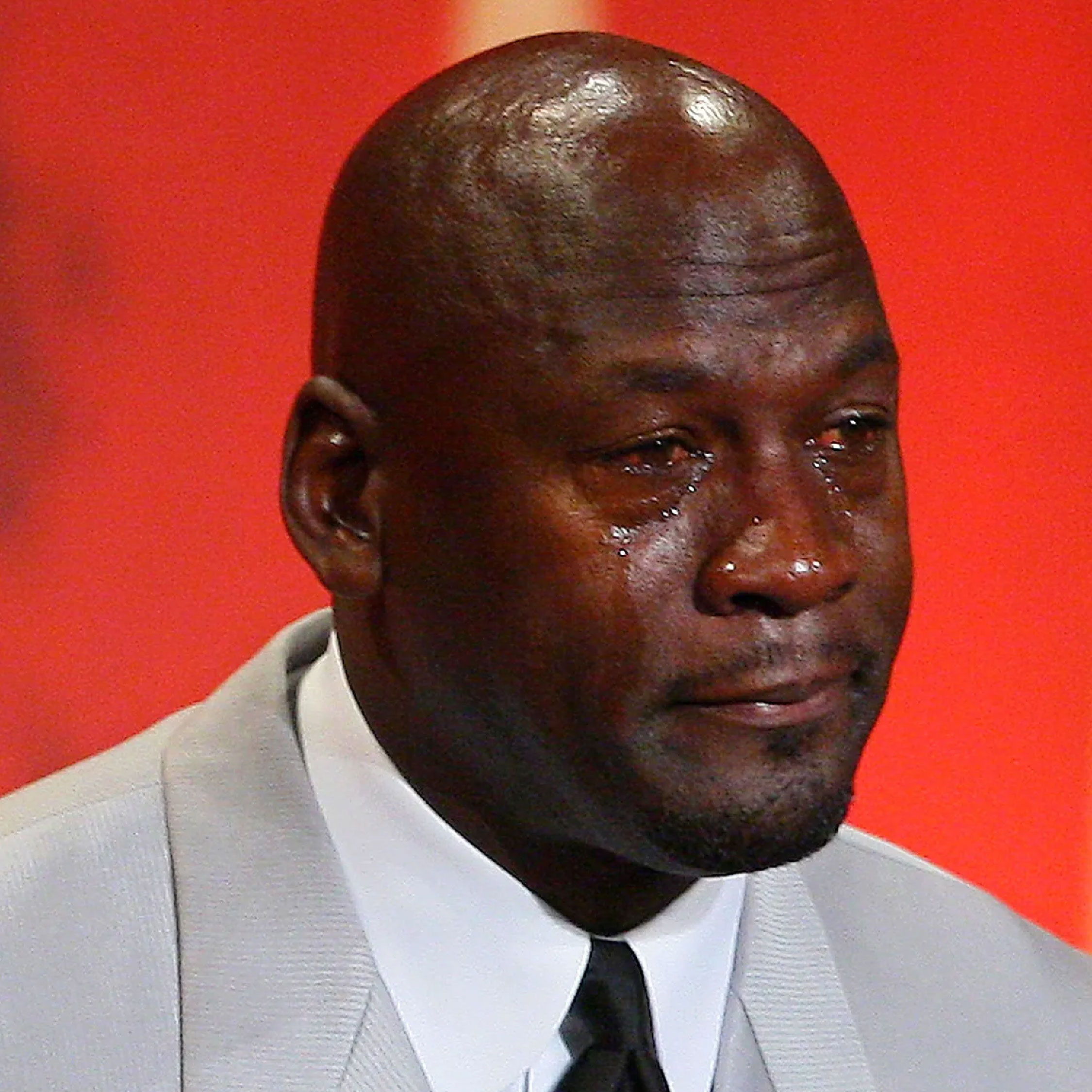 Man in a suit with tears, looking emotional against a red background.