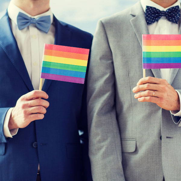 Two men in bowties holding up a gay pride flag
