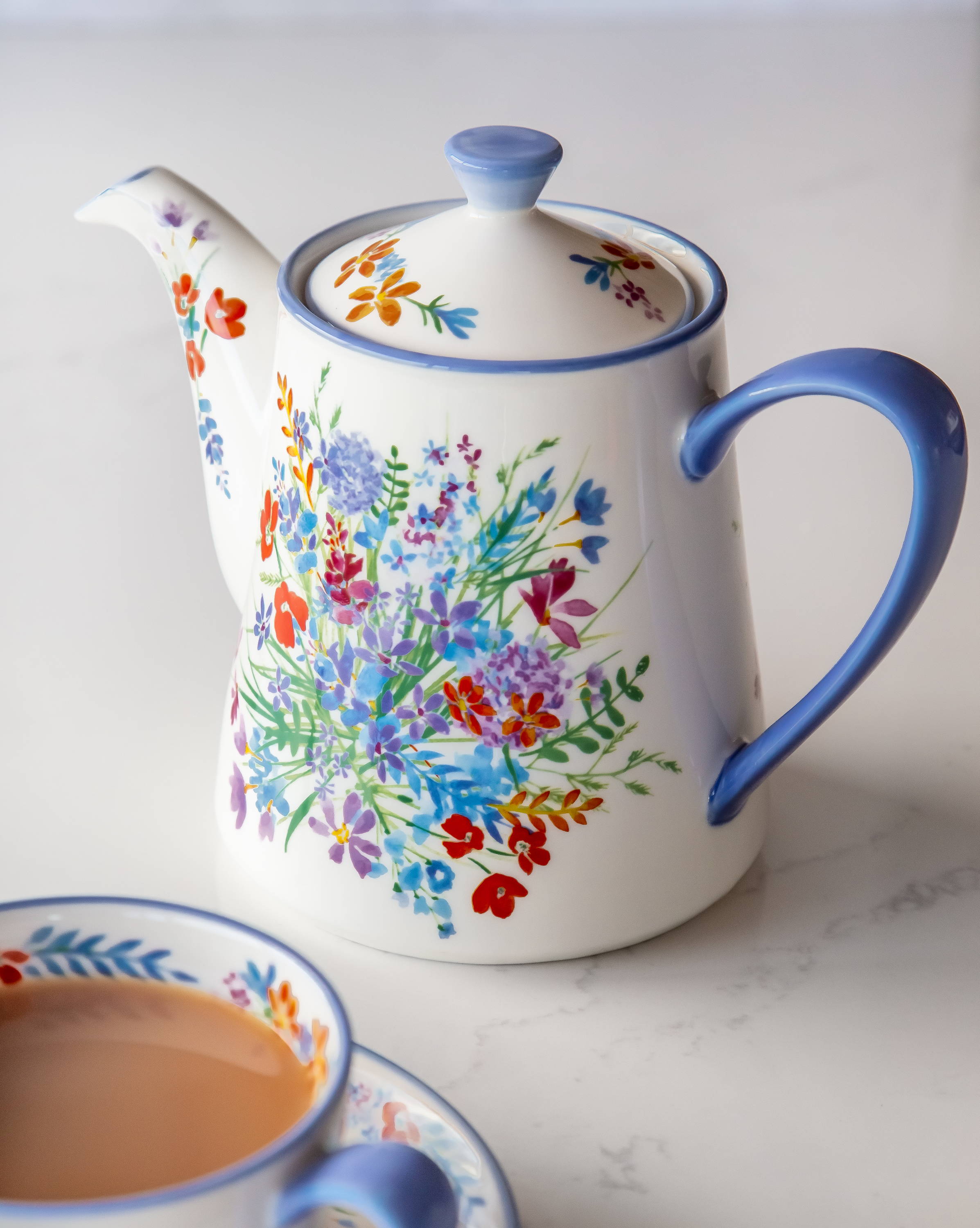 A teapot with a floral design and a cup of tea next to it.