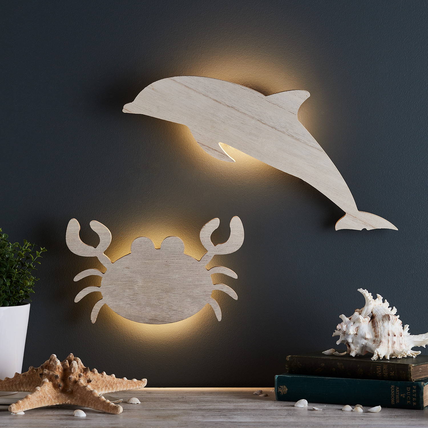 Dolphin and grab wooden wall lights againsts a navy wall with a starfish and shells on the table beneath.