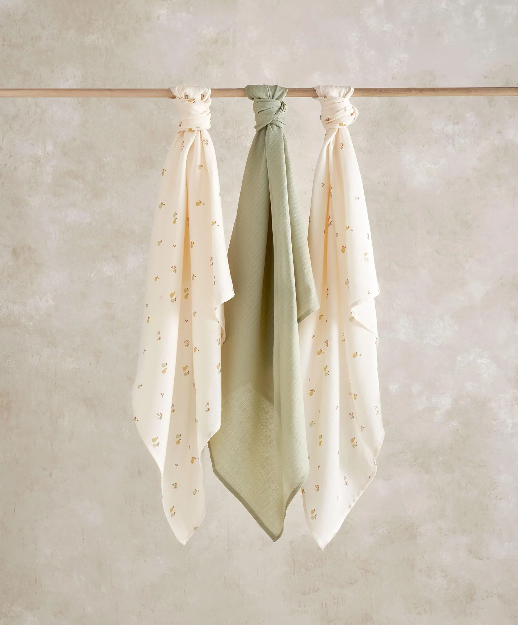 Three scarves hanging on a wooden rod against a textured background.