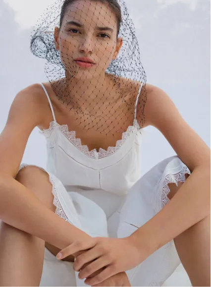 Model in white outfit with a veil, sitting against a light background.