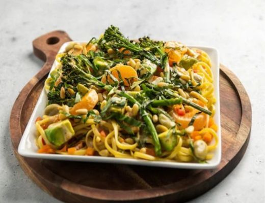 A plate of pasta with vegetables and herbs on a wooden board.