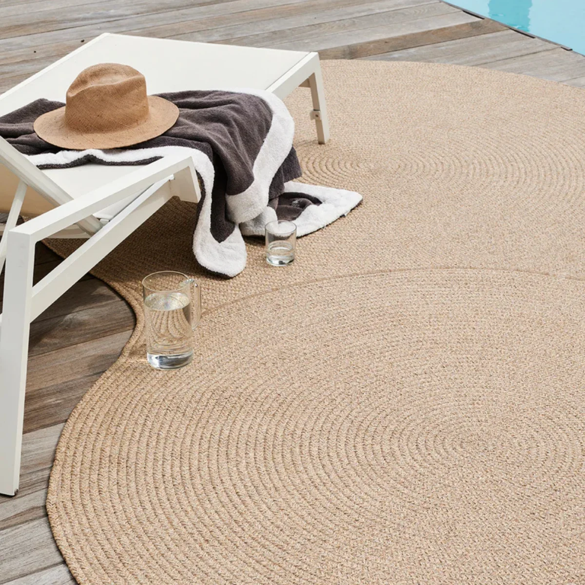 Irregular-shaped woven outdoor rug beside a pool with lounge chairs, showcasing a weather-resistant rug ideal for pool decks and sunny outdoor spaces. 