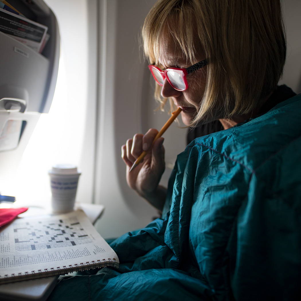Woman doing crossword on a plane with a blanket